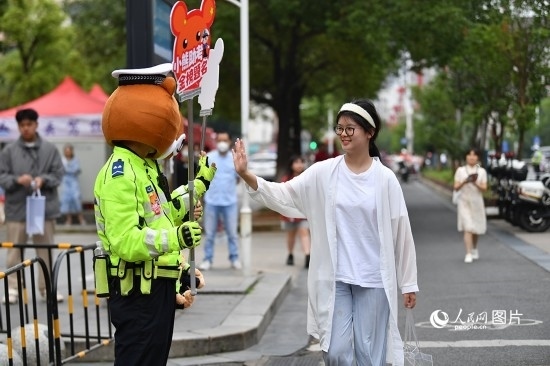 6月7日上午9時，隨著鈴聲的響起，2023年江西高考正式開考，江西省的53.57萬考生以縣（區(qū)）為單位隨機安排在全省256個考點、18968個考場參加高考。圖為“小熊交警”和考生擊掌鼓勵。 人民網(wǎng)記者 時雨攝