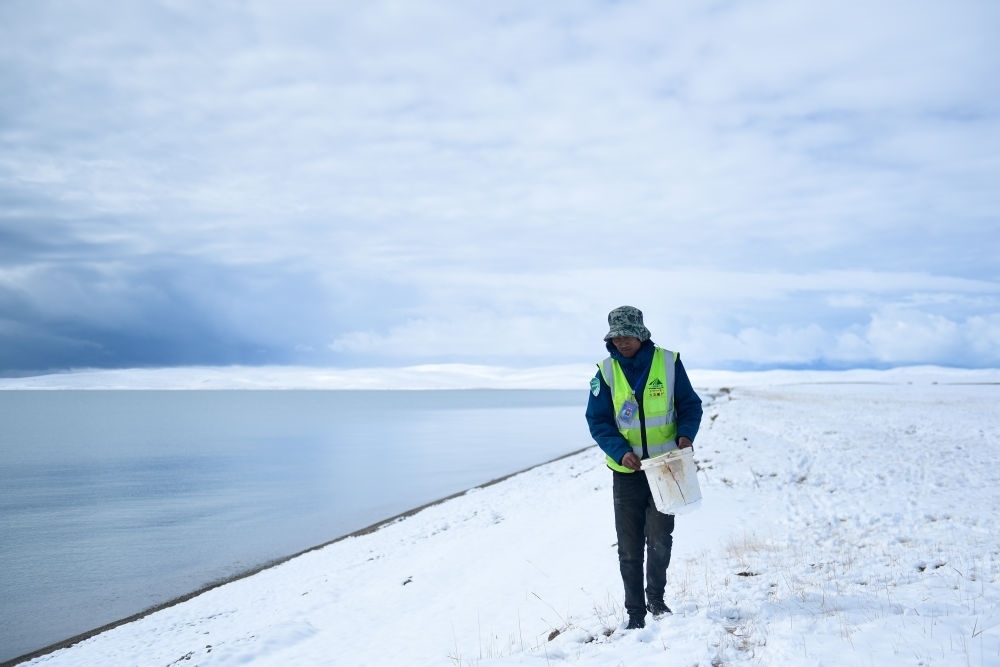 2021年10月20日，在青海省果洛藏族自治州瑪多縣扎陵湖鄉(xiāng)勒那村，三江源國家公園黃河源園區(qū)生態(tài)管護(hù)員在扎陵湖邊撿拾垃圾。新華社記者 張龍 攝