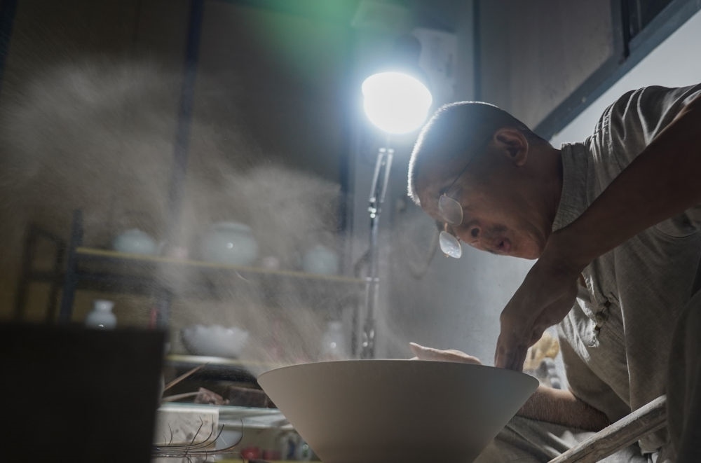 ↑ 在景德鎮(zhèn)，手工匠人吹去坯內(nèi)的泥土（2021年7月14日攝）。