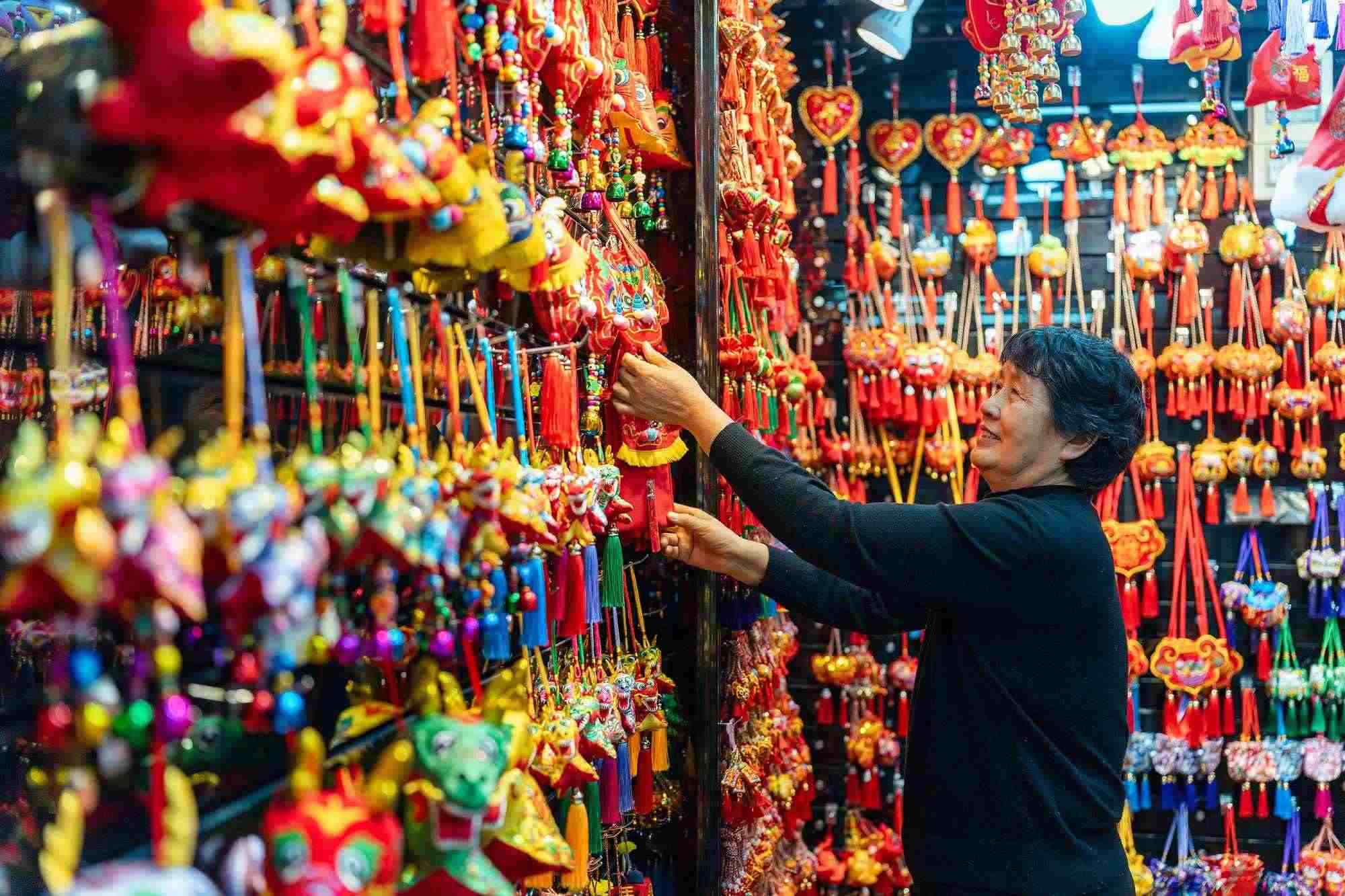 2023年12月11日，金華義烏國(guó)際商貿(mào)城，龍年喜慶用品掛滿攤位，顧客正在挑選中。