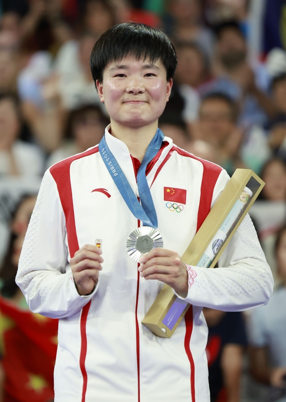 巴黎奧運(yùn)會(huì)羽毛球女子單打亞軍、中國選手何冰嬌在頒獎(jiǎng)儀式上一手握著銀牌，一手握著西班牙奧委會(huì)徽章（2024年8月5日攝）。新華社記者 任正來 攝