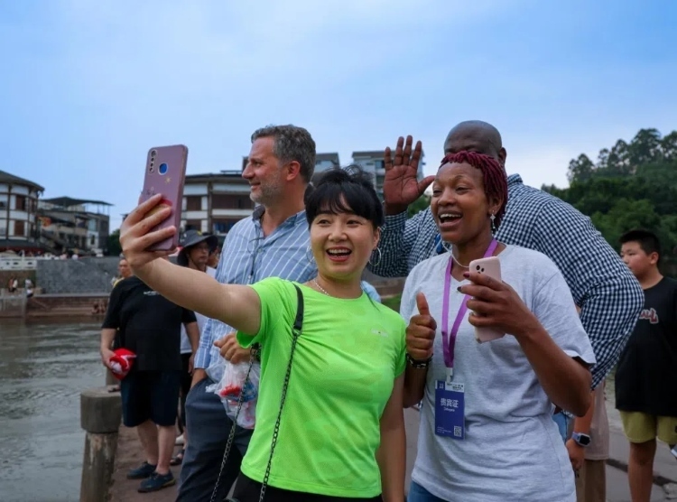 2024“一帶一路”媒體合作論壇聯(lián)合采訪調(diào)研行成員在樂山蘇稽古鎮(zhèn)與游客合影留念。本報(bào)記者 伊霄攝