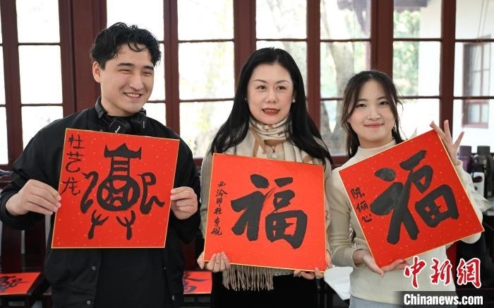 1月20日，外籍留學(xué)生和西泠印社社員李硯(中)展示各自創(chuàng)作的福貼。當(dāng)日，來(lái)自巴西、馬來(lái)西亞、加納、哈薩克斯坦的外籍留學(xué)生在浙江杭州西泠印社體驗(yàn)福貼、春聯(lián)和篆刻，感受古老的中國(guó)傳統(tǒng)文化。中新社記者 王剛 攝